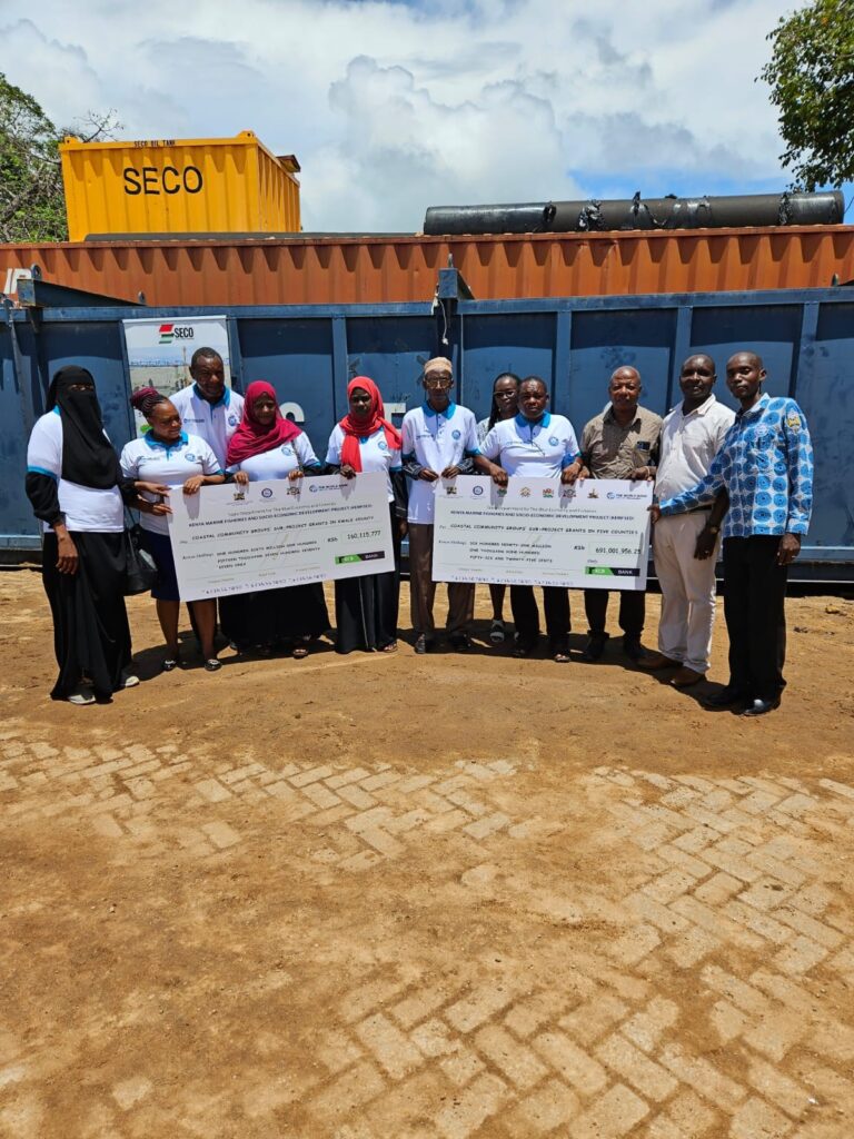 KEMFSED National Project Coordinator Patrick Kiara and other project officials join community representatives to show the cheques for the latest disbursement of grants for community projects