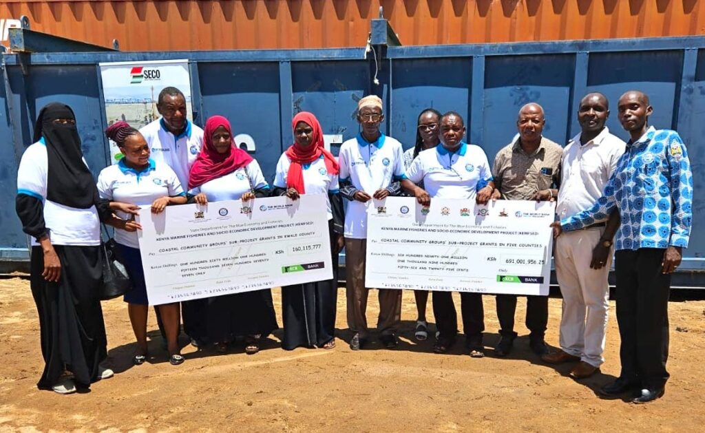 KEMFSED National Project Coordinator Patrick Kiara and other project officials join community representatives to show the cheques for the latest disbursement of grants for community projects