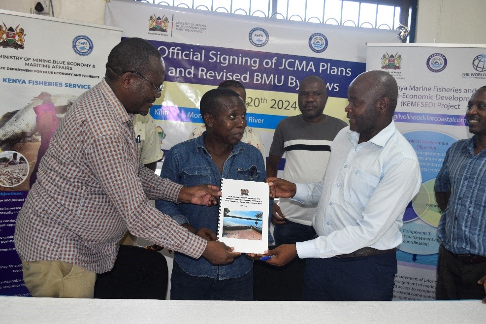 Kenya Fisheries Service Director General Daniel Mungai hands over a JCMA plan to Kilifi County CECM for fisheries Dr Chula Mwagona and a representative of BMUs